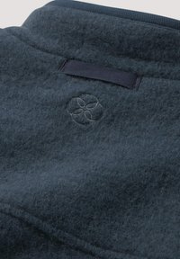 Donkerblauwe viltstof met een zachte textuur, gekenmerkt door een tonale geborduurde bloemenembleem en een contrasterende marineblauwe geribbelde kraag.