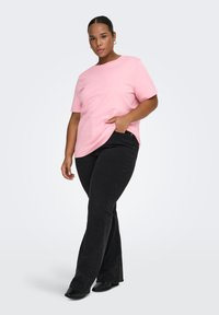 Lyserød bomuld t-shirt med løs pasform, rund halsudskæring og korte ærmer, kombineret med sorte flare jeans og sorte støvler med hæl.