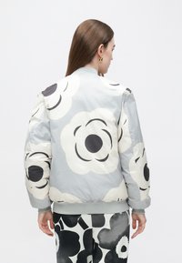 Jasnoszara bomberka z dużymi czarno-białymi motywami kwiatowymi, z prążkowanymi mankietami i krawędzią, o gładkiej, błyszczącej fakturze.