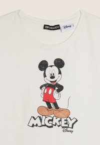 Camiseta blanca de algodón con un gráfico desgastado de Mickey Mouse en pantalones cortos rojos y zapatos amarillos, con el nombre "MICKEY" impreso abajo.