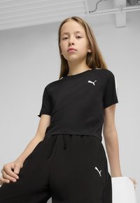 Crni skraćeni T-shirt s bijelim Puma logotipom i kontrastnim prugastim detaljima; uparen s crnim trenirkama koje imaju isti logotip.