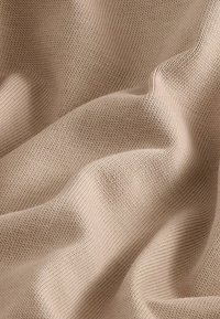 Tejido de punto beige con una superficie lisa y texturizada, que presenta un suave canalé y un caimiento blando, creando suaves ondas a lo largo del material.