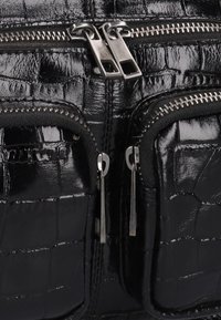 Zwarte krokodillenleer tas met twee ritsvakken aan de voorkant, metalen hardware en een gestructureerde afwerking. De ritsen hebben dubbele trekstangen.
