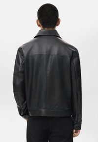 Giubbotto in pelle nera con colletto classico, texture liscia e design con spacco posteriore. Presenta polsini con bottone e una vestibilità sartoriale.