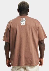 Brown cotton t-shirt with a relaxed fit, featuring a white graphic design on the upper back with the text "Rocawear 1999."