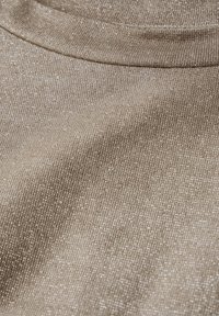 Beige textil med en subtil glans och tät väv, som visar en böjd söm och mjuka veck.