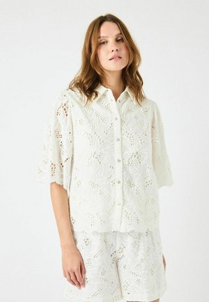 Hvit brodert skjorte med kort erme, preget av intrikate blomsterdesign og bølgete kanter, parret med matchende shorts.