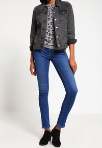 Chaqueta de mezclilla gris sobre una camisa gris con estampado de leopardo, combinada con jeans skinny azules y botas negras de tobillo. Colores sólidos y patrones distintos.