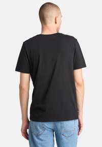 Camiseta de algodón negra con mangas cortas, escote redondo y un corte relajado. Etiqueta visible en la costura lateral izquierda. Combinada con jeans de color azul claro.
