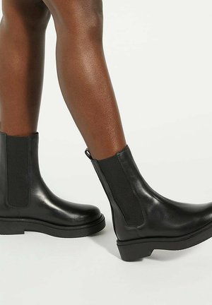 Zwarte leren enkelboots met elastische zijkanten, een gladde afwerking en een chunkyrubber zool, met een trekband aan de achterkant.