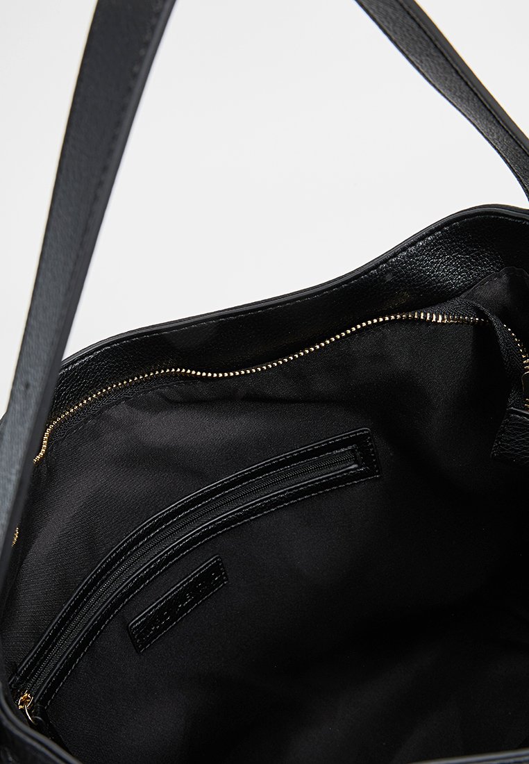 Intérieur d'un sac à main en cuir noir avec une texture lisse, doté d'une fermeture éclair dorée, d'une doublure en tissu noir et d'une poche zippée.