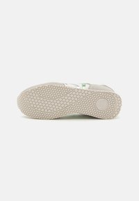 Helle graue Sneaker-Sohle mit einem Wabenmuster, strukturiertem Gummi und einer runden Form. Verfügt über ein kreisförmiges Logo-Detail im Fersenbereich.