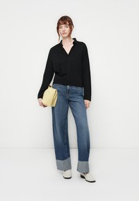 Black long-sleeve top with a collar, blue wide-leg jeans with gray cuffs, and a yellow handbag. White ankle boots complete the outfit.
