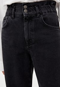 Jean en denim noir avec taille haute, fermeture à deux boutons, passants pour ceinture et poches avant. Texture lisse et coupe ajustée.