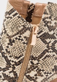 Stivale alla caviglia in pelle di serpente con un motivo texturizzato beige e nero, hardware della cerniera dorato e fodera interna liscia.