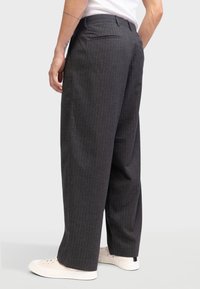 Tumed hallid triibulised püksid, millel on mugav lõige, ühe tagatasku ja stiliseeritud valgete tossudega.