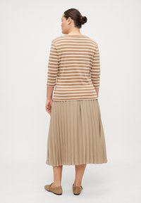 Gestreiftes braun-weißes Oberteil mit Dreiviertelärmeln, kombiniert mit einem plissierten beigen Rock, beide aus weichen Stoffen und fließenden Designs gefertigt.
