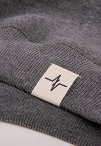 Grijze ribbelstof met een label waarop een zwart bliksemschicht-logo staat. De textuur is zacht en benadrukt het geweven patroon.