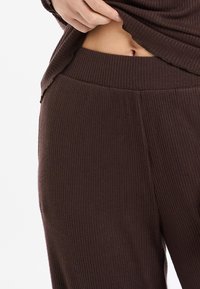 Braune, gerippte Freizeitkleidung aus Stoff mit einem breiten, elastischen Bund. Nahaufnahme zeigt weiche Textur und lockere Passform.