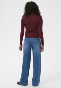 Burgundy long-sleeve top paired with light blue wide-leg denim jeans. Textured knit fabric, relaxed fit, and classic blue denim wash.
