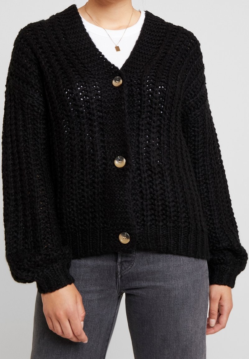 Svart stickad cardigan med ett strukturerat mönster, djup V-hals, långa ärmar och stora beige knappar, med ribbad mudd och fåll.