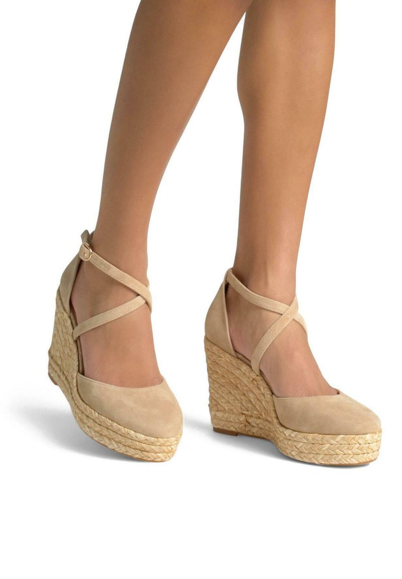 Sandales à talons compensés en daim beige avec des brides entrecroisées à la cheville, des détails en corde tressée sur le talon compensé et un design à bout rond.