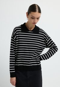 Pullover a righe bianche e nere con colletto di perline nere, caratterizzato da maniche lunghe e una vestibilità rilassata, realizzato in un morbido tessuto strutturato.