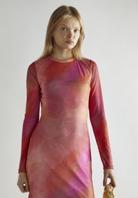 Długo-sleeve, dopasowana sukienka w gradientowych odcieniach czerwieni i różu. Miękka, gładka tekstura z okrągłym dekoltem i detalami przy dolnym szwie.