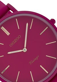 Montre analogique fuchsia avec une finition mate, des marqueurs d'heure dorés, des aiguilles fines et un boîtier rond. Présente le logo "oozoo" et le texte "Vintage".
