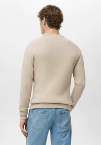 Beige geribbelde trui met lange mouwen en een ronde hals, een losse pasvorm en een aangesloten zoom, gedragen met blauwe spijkerbroek, achteraanzicht.