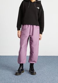 Felpa cropped nera a maglia waffle con logo frontale; pantaloni larghi viola chiaro con cintura elastica e piccolo logo silver; stivali neri con lacci.