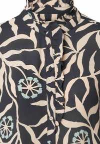 Bluzka we wzory z marszczonym kołnierzykiem, w kolorach granatowym, kremowym i morskim, z zapięciem na guziki i botanicznym nadrukiem. Materiał o fakturze.