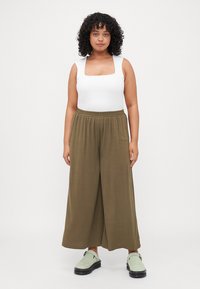 White square-neck bodysuit with olive green wide-leg trousers, featuring an elastic waistband and soft texture. Footwear: light green clogs.