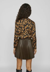 Blusa con stampa leopardata a maniche lunghe, abbinata a una gonna plissè in finta pelle marrone. L'outfit presenta una vita elastica e un tessuto strutturato.