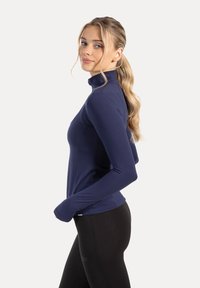 Donkerblauw sportief top met lange mouwen, een hoge kraag en een nauwsluitend ontwerp, gemaakt van een glad, rekbaar materiaal. Gecombineerd met zwarte legging.