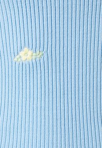 Světle modrá pletená látka s vertikálním vroubkováním, která má uprostřed jemně vyšívané květiny v žluté a zelené barvě.