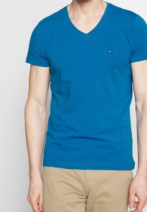 Blaues V-Ausschnitt-T-Shirt aus Baumwolle mit kleinem Logo auf der Brust. Kurze Ärmel und taillierte Passform. Glatte Textur.