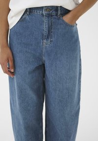 Jeans in denim blu chiaro, a vita alta, con una vestibilità rilassata, dotati di tasche laterali e dettagli di cucitura sottili. Tessuto morbido, gambe dritte.