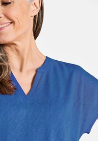 Blauwe V-hals T-shirt van zachte stof met korte mouwen, voorzien van een lichte kraag en een relaxte pasvorm. De textuur lijkt glad en licht van gewicht.