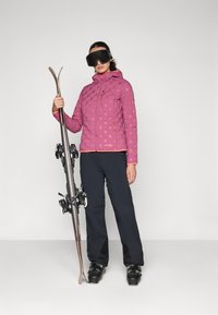 Ροζ μπουφάν με επένδυση και σχέδιο, με φερμουάρ μπροστά και κουκούλα; μαύρα σκι παντελόνια; κρατώντας σκι; φοράει μεγάλες μαύρες γυαλιές.