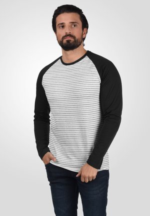 Camiseta de manga larga con un cuerpo blanco y rayas horizontales negras, y mangas raglán negras. Tejido suave con un ajuste relajado.