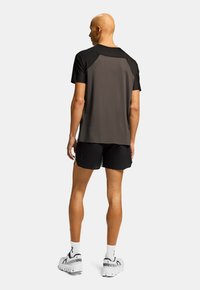Conjunto atlético masculino que incluye una camiseta negra de manga corta con la parte trasera texturizada en gris y pantalones cortos negros. Unos zapatos deportivos blancos y negros completan el look.