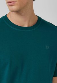 Aquamarine katoenen t-shirt met een ronde hals en korte mouwen, met een subtiele logo in de linkerbovenhoek en een gladde textuur.