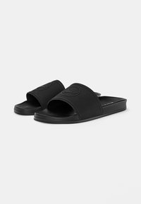 Sorte slides lavet af tekstureret gummi med en bred rem, der har et rundt logo. SÅlen er flad og let kontureret for komfort.