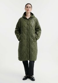 Giubbotto imbottito verde oliva, trapuntato, con cappuccio, bottoni frontali e ampie tasche laterali. Materiale liscio e lucido con una trama morbida.