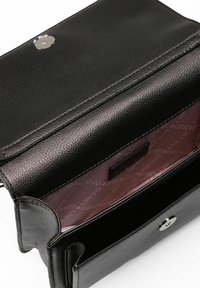 Bolso de mano de cuero negro con exterior texturizado. El interior cuenta con un forro malva con un patrón de logotipos y un cierre magnético frontal.