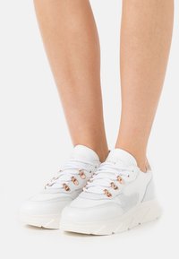 Białe sneakersy z teksturowaną skórzaną cholewką, szarymi akcentami i różowo-złotymi detalami. Posiadają grube podeszwy i tradycyjny system sznurowania.