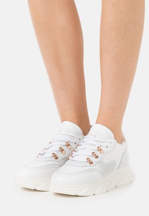 Sneakers bianchi con tomaia in pelle testurizzata, dettagli grigi e accessori in oro rosa. Dotati di suole spesse e sistema di allacciatura tradizionale.