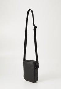 Sort firkantet crossover taske lavet af tekstureret læder med en lang, justerbar rem og en lynlåslukning. Minimalistisk design.
