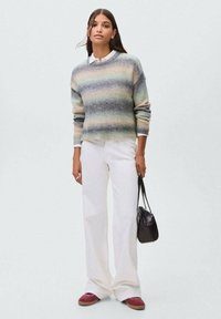 Pleteni pulover s horizontalnim črtastim vzorcem v nežnih odtenkih zelene, sive in bež; v kombinaciji z belimi širokimi hlačami in rdečimi supergami.